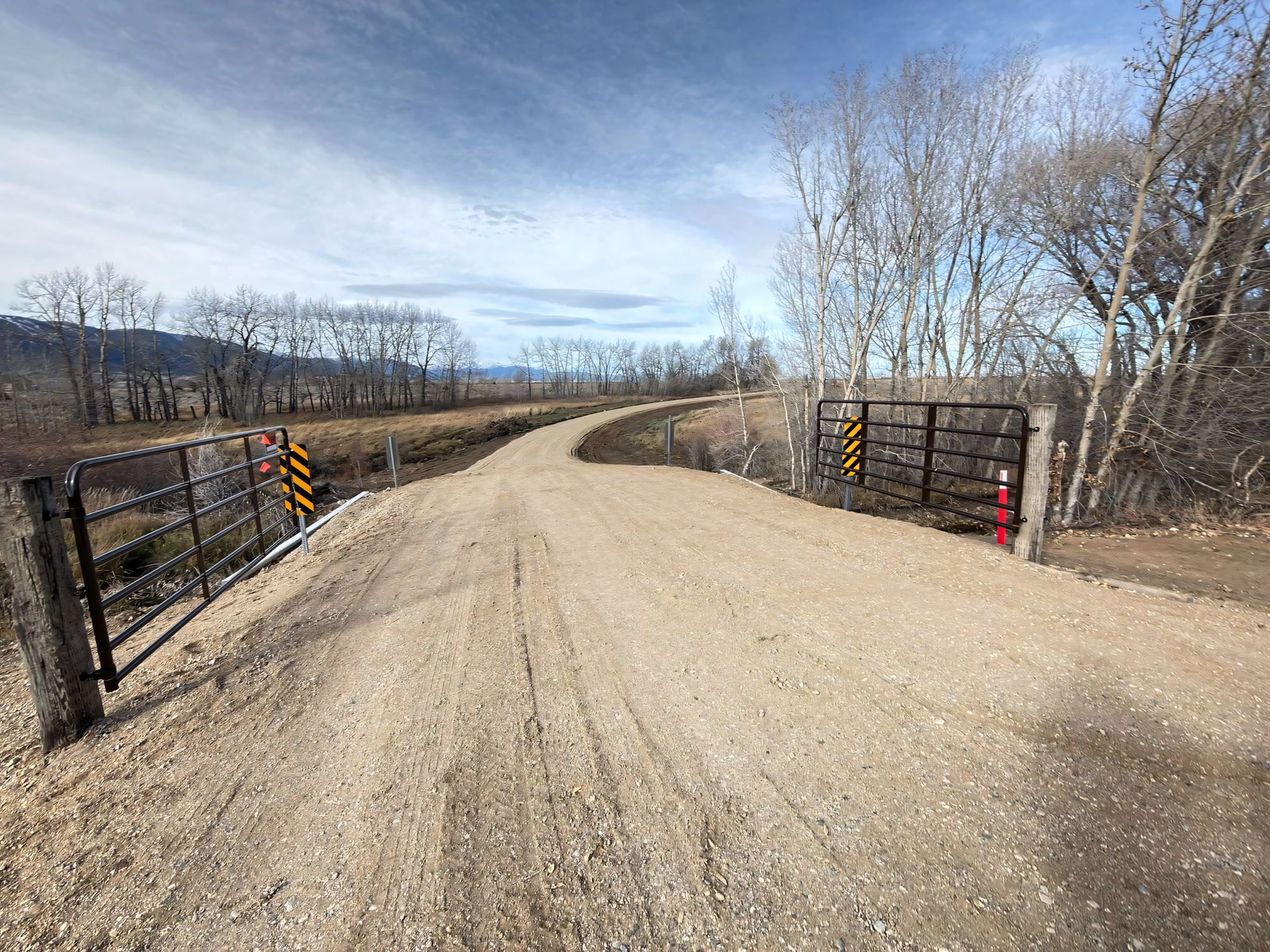 Fresh gravel road curving between open gates toward the Beartooth Mountains